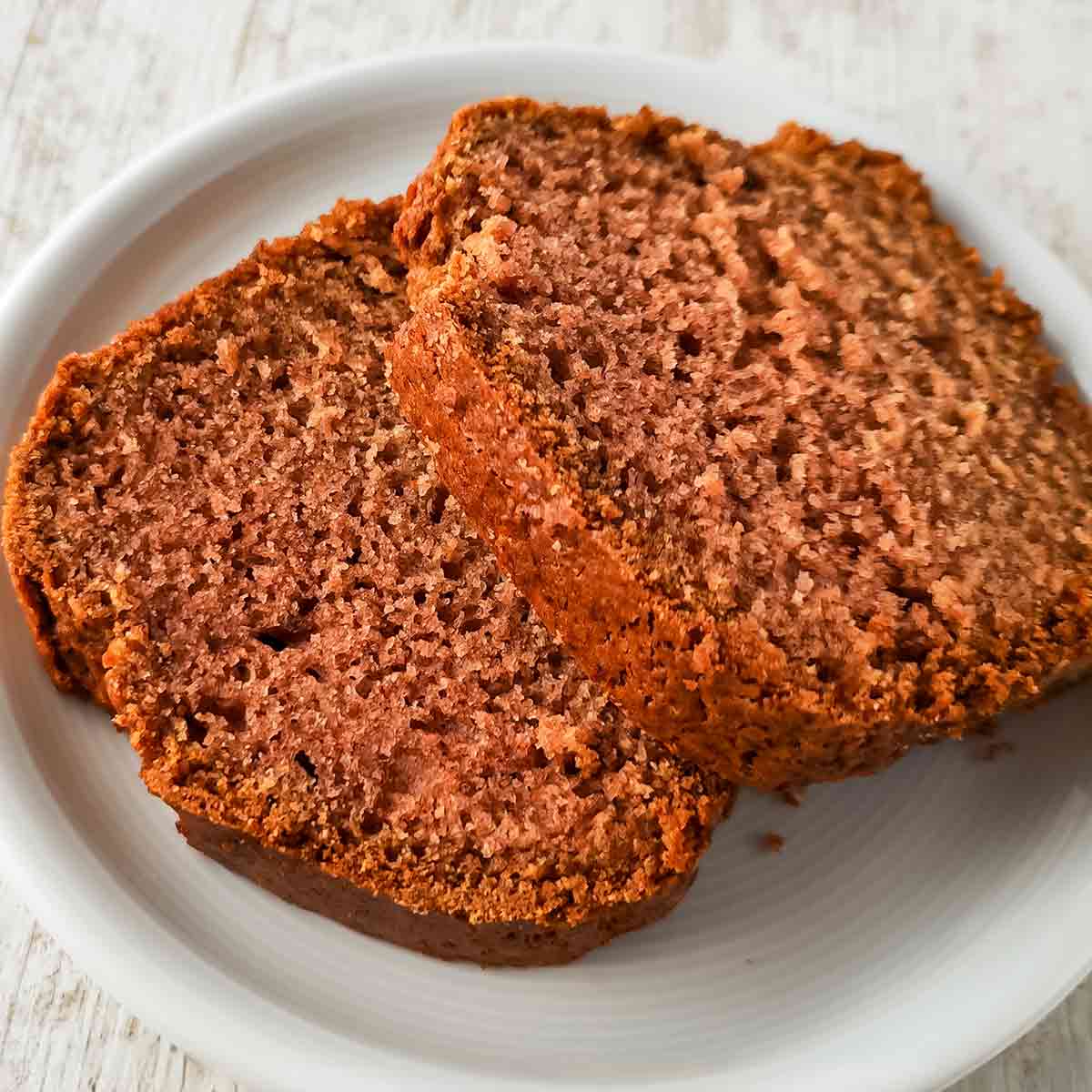 Zwei saftige Scheiben veganer Rührkuchen mit Apfelmus auf einem weißen Teller.