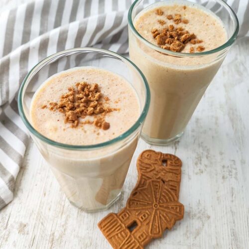 Ein Glas mit veganem Spekulatius-Milchshake und Spekulatiusbröseln auf der Oberfläche, ein zweites Glas ist im Hintergrund zu sehen.