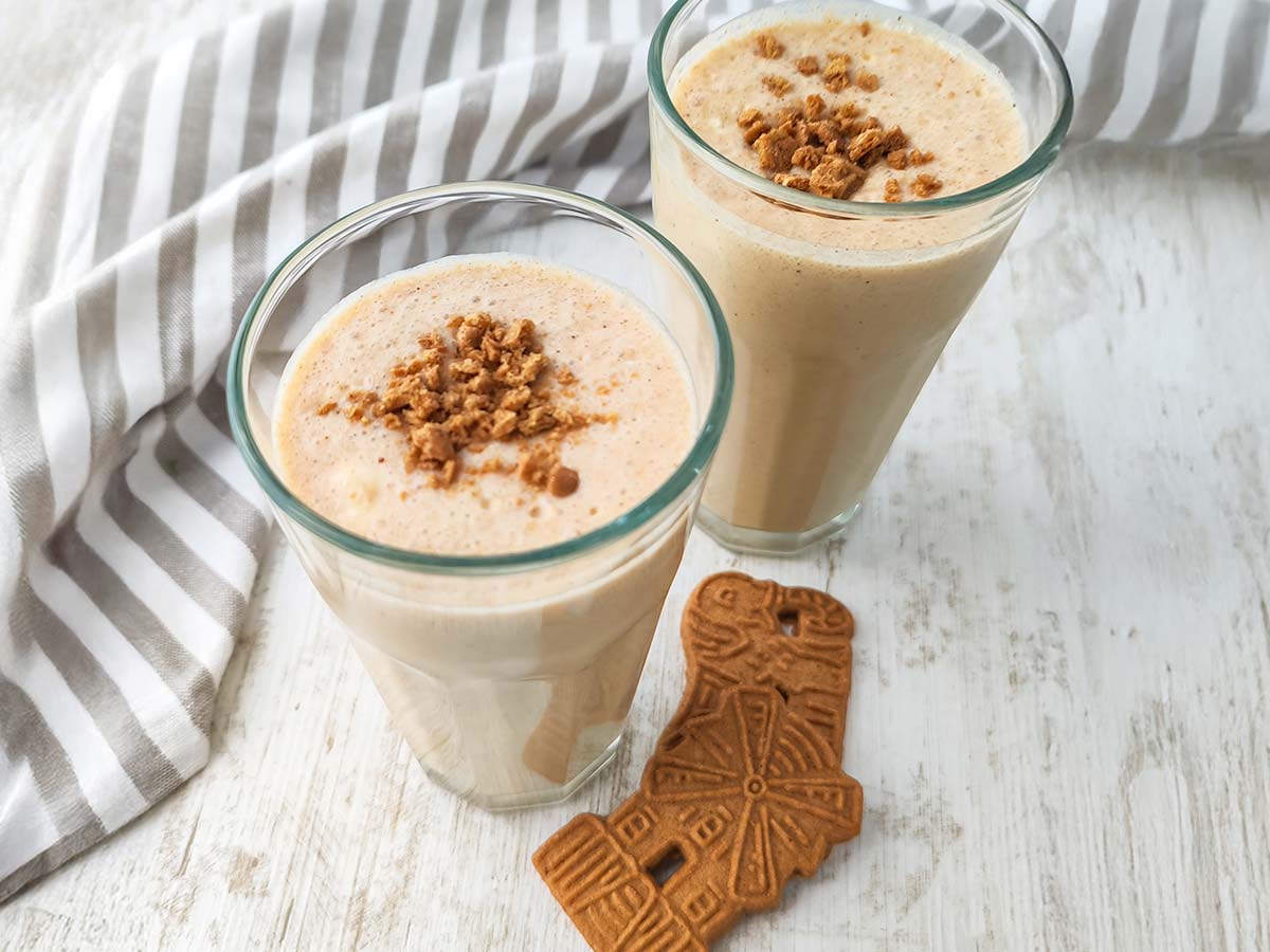 Ein Glas mit veganem Spekulatius-Milchshake und Spekulatiusbröseln auf der Oberfläche, ein zweites Glas ist im Hintergrund zu sehen.