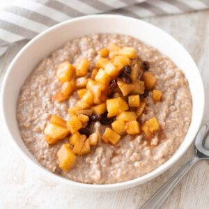 Veganer Apfel-Zimt-Porridge mit Apfelstücken in einer weißen Schüssel.