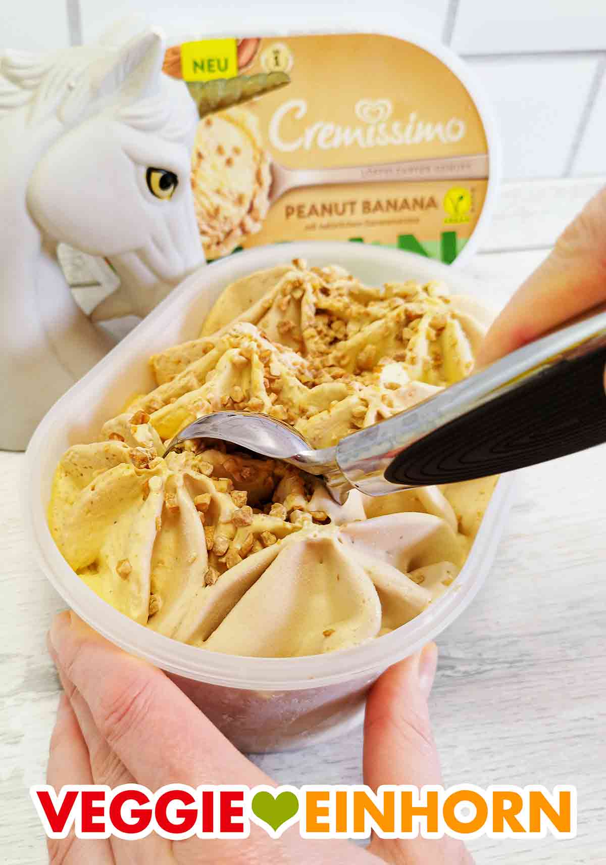 Hier sieht man schon, wie cremig und sahnig die vegane Eiscreme von Cremissimo ist. Eine Kugel veganes Cremissimo Peanut Banana wird mit einem Eisportionierer aus der Packung entnommen.