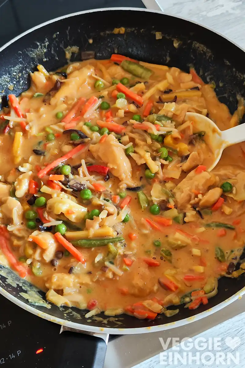 Nahaufnahme von cremigem veganem Hähnchen Curry in Erdnuss-Kokos-Soße mit buntem Wok-Gemüse in einer Pfanne auf dem Herd.