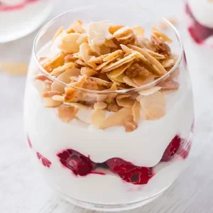 Veganes Himbeer-Dessert im Glas, geschichtet mit weißer Creme und tiefgekühlten Himbeeren, bestreut mit karamellisierten Mandelblättchen.