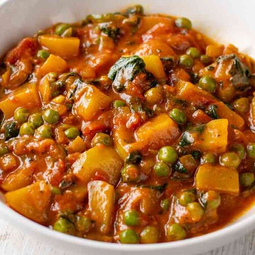 Teller mit veganem Kartoffelcurry mit Spinat und Erbsen