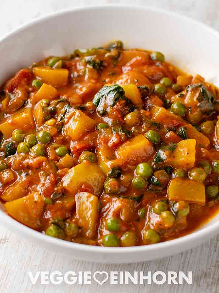 Teller mit veganem Kartoffelcurry mit Spinat und Erbsen