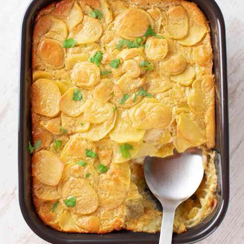 Auflaufform mit veganem Kartoffelgratin mit Cashewmus und einem Servierlöffel