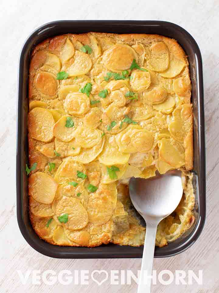 Auflaufform mit veganem Kartoffelgratin mit Cashewmus und einem Servierlöffel