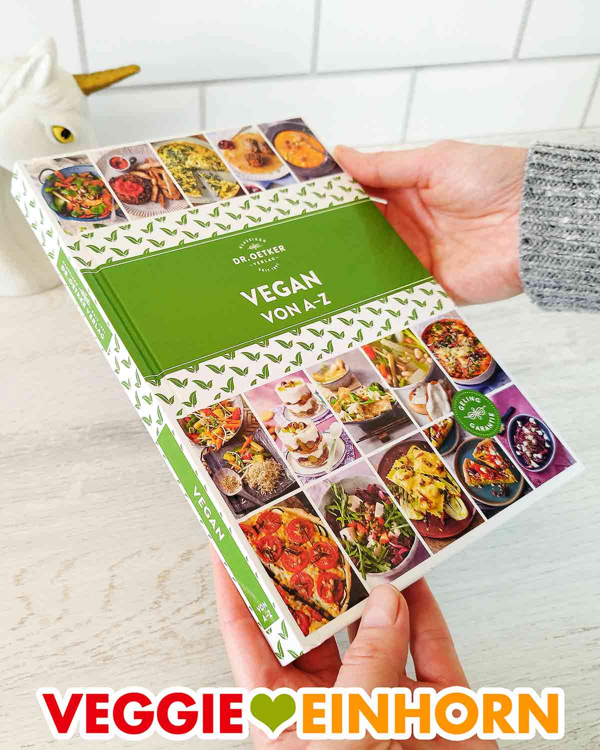Vorderseite des Buches Vegan von A - Z von Dr. Oetker Hände halten das Kochbuch Vegan von A bis Z von Dr. Oetker