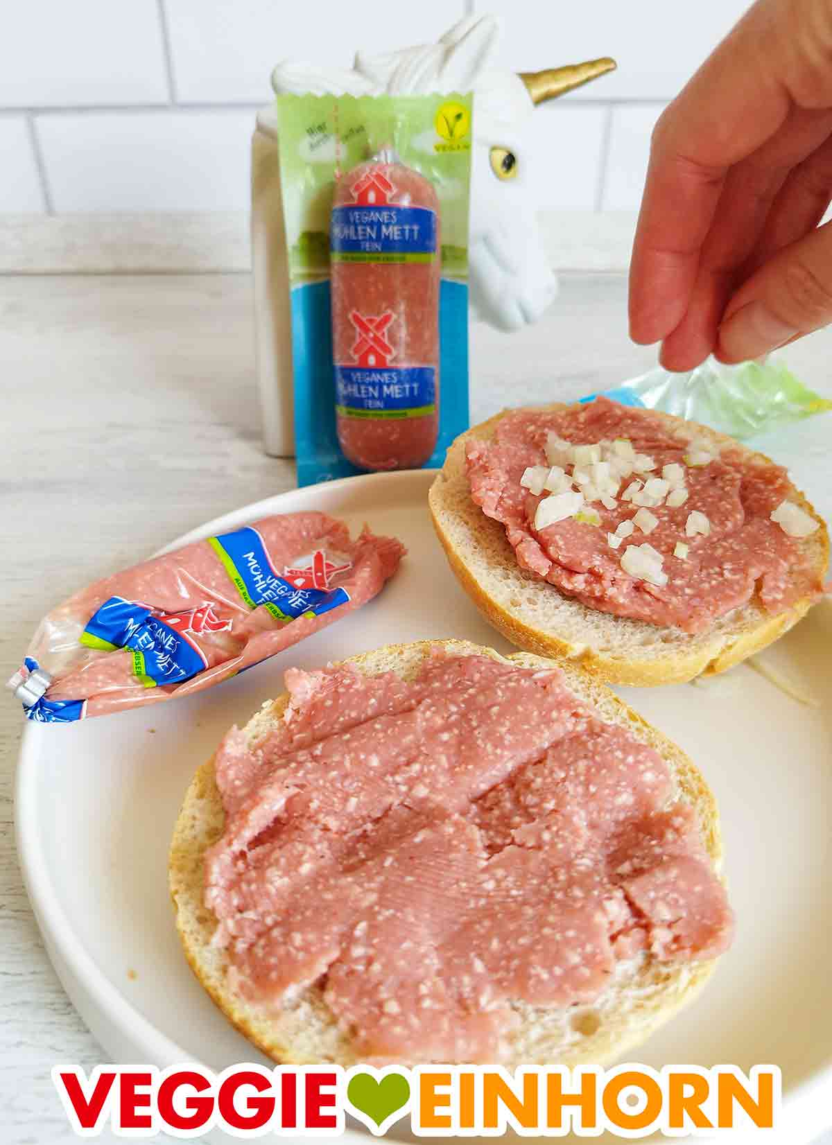 Zwei Brötchen mit veganem Mett von Rügenwalder Mühle und Zwiebeln Die veganen Mettbrötchen werden mit Zwiebelwürfeln bestreut