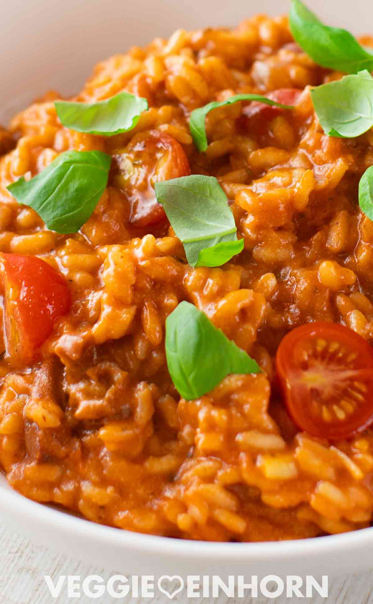 Nahaufnahme von veganem Tomatenrisotto mit Kirschtomaten und frischem Basilikum, angerichtet in einer weißen Schale.