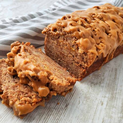Anschnitt eines veganen Spekulatius Bananenbrots mit Karamellglasur auf einem hellen Holztisch, daneben ein gestreiftes Tuch.