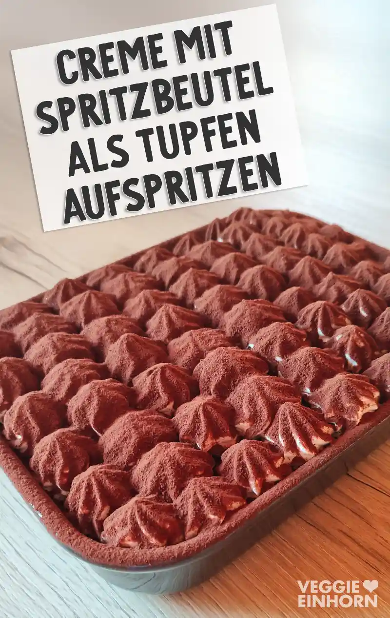 Veganes Tiramisu in einer rechteckigen Form mit gleichmäßig aufgespritzten Creme-Tupfen, bestäubt mit Kakaopulver.