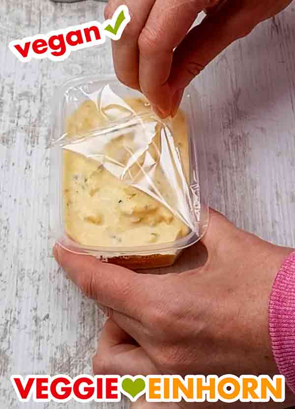 Wir packen den veganen Eiersalat aus. Die Folie der Verpackung des veganen Eiersalates wird abgezogen.