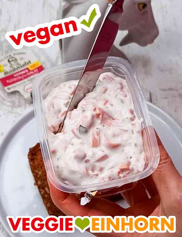 Der Feinkostsalat enthält vegane Fleischwurst, vegane Mayonnaise und Gewürzgurken. Der vegane Fleischsalat von Popp Feinkost in der geöffneten Packung mit einem Messer