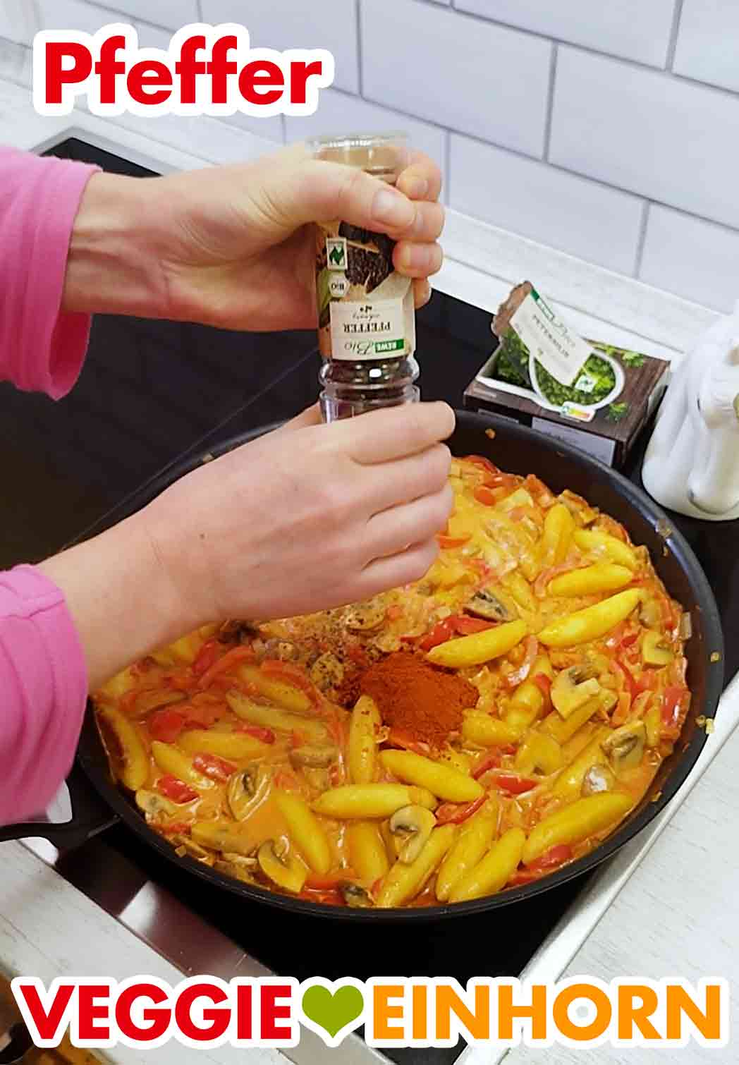 Das Gericht wird mit schwarzem Pfeffer gewürzt. Cayennepfeffer geht auch. Zwei Hände halten eine Pfeffermühle über die vegane Schupfnudelpfanne