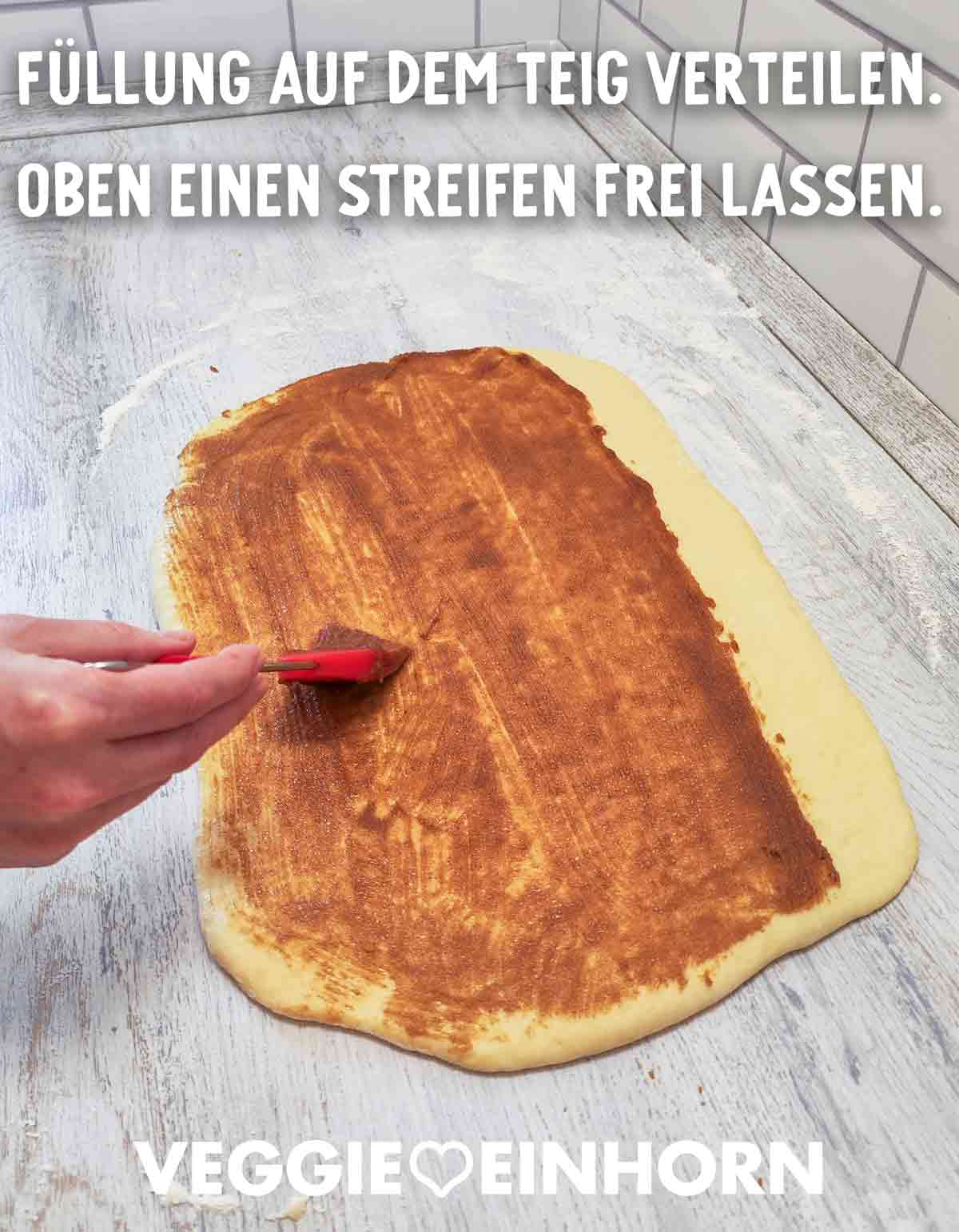 Zimtfüllung wird mit einem Silikonpinsel auf ausgerolltem Hefeteig verteilt.