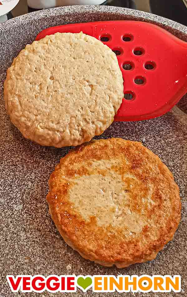 Die veganen Chicken Burger von The Vegetarian Butcher werden in der Pfanne gewendet. Wenden der veganen Sieht-Chick-Aus Burger mit dem Pfannenwender
