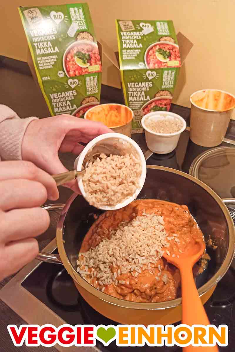 Der gekochte Naturreis aus dem Becher wird in den Topf zu der Tikka Masala Soße und dem veganen Fleischersatz gegeben. Der Reis wird in den Topf zugefügt.