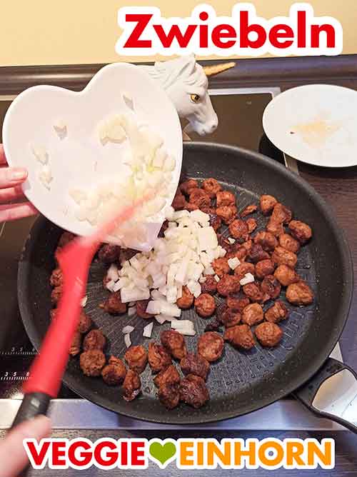 Zufügen der Zwiebeln für das vegane Gulasch Zwiebeln werden in die Pfanne zugefügt