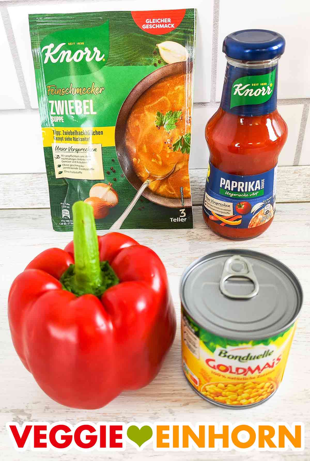 Knorr Zwiebelsuppe, Knorr Paprikasauce Ungarische Art, Paprikaschote, Bonduelle Goldmais Eine Tüte vegane Zwiebelsuppe, eine Flasche vegane Paprikasauce Ungarische Art, rote Paprika, kleine Dose Mais